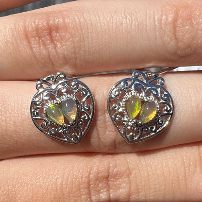 A pair of dangling sterling silver filigree heart earrings, each set with two Ethiopian opals.