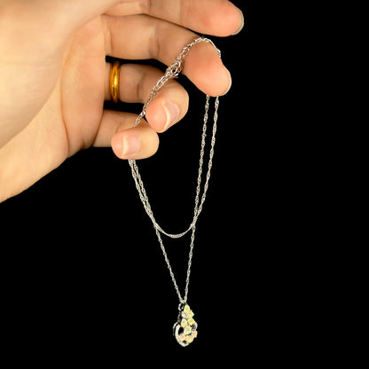 A silver Ethiopian opal necklace dangling from a hand by its chain against a black backdrop.