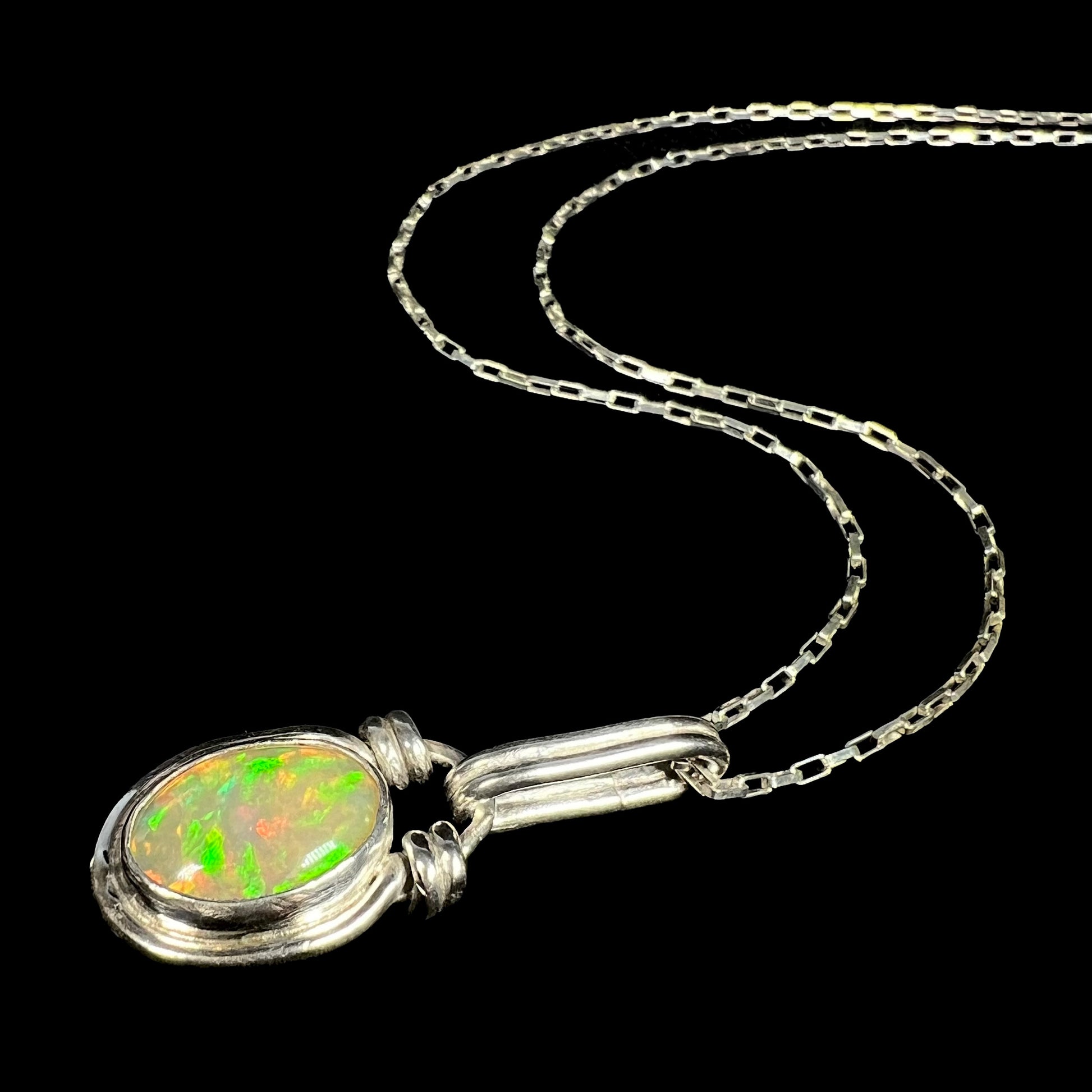 A sterling silver Ethiopian opal necklace with green fire, shown from an angle laying against a black backdrop.