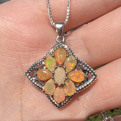 A sterling silver Ethiopian opal necklace shown close-up in the sunlight, held in a hand.  The opals are orange and green.