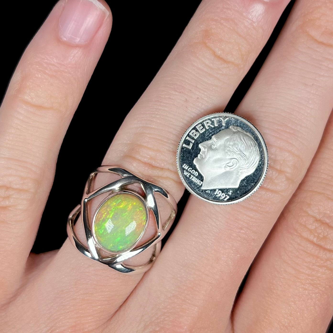 A sterling silver Ethiopian opal ring with green color play, worn on a hand next to a dime coin for scale.