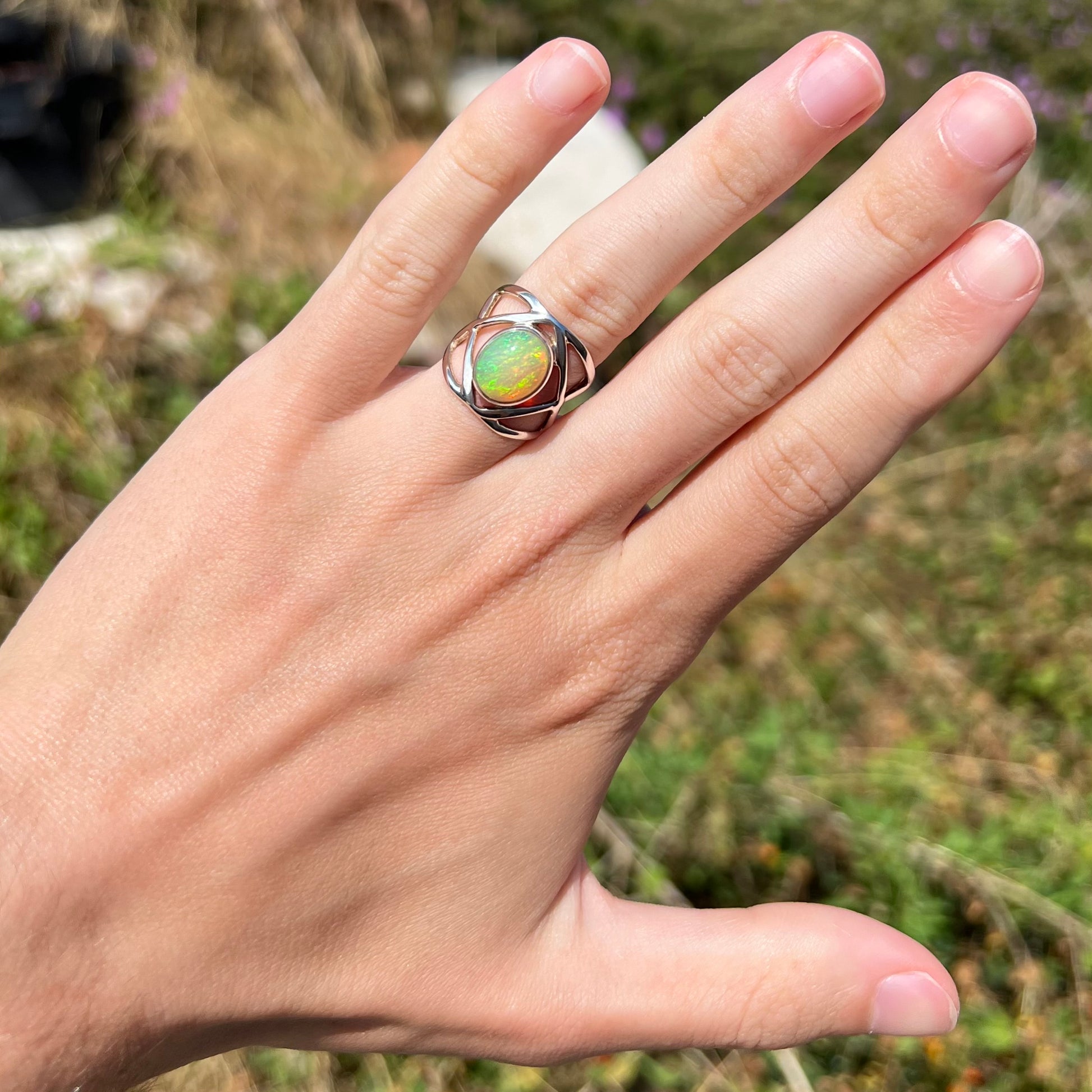 A sterling silver Ethiopian opal ring worn on a hand, shown at a distance in the sunlight.