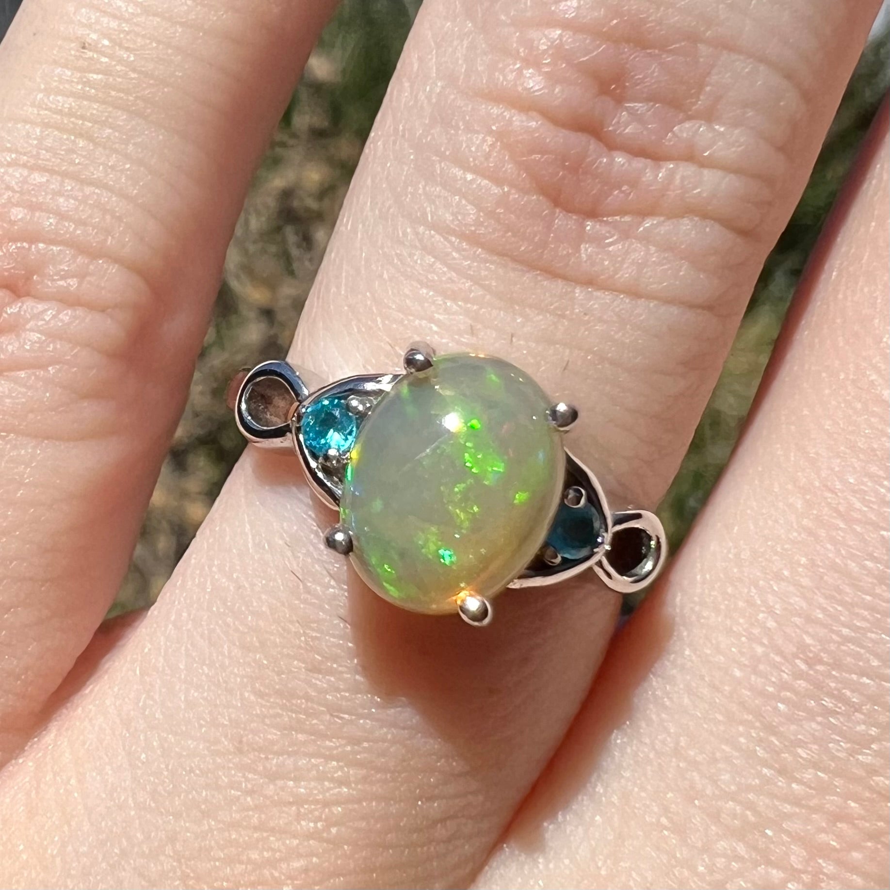 Close-up of sterling silver Ethiopian opal and blue apatite ring in natural light on finger