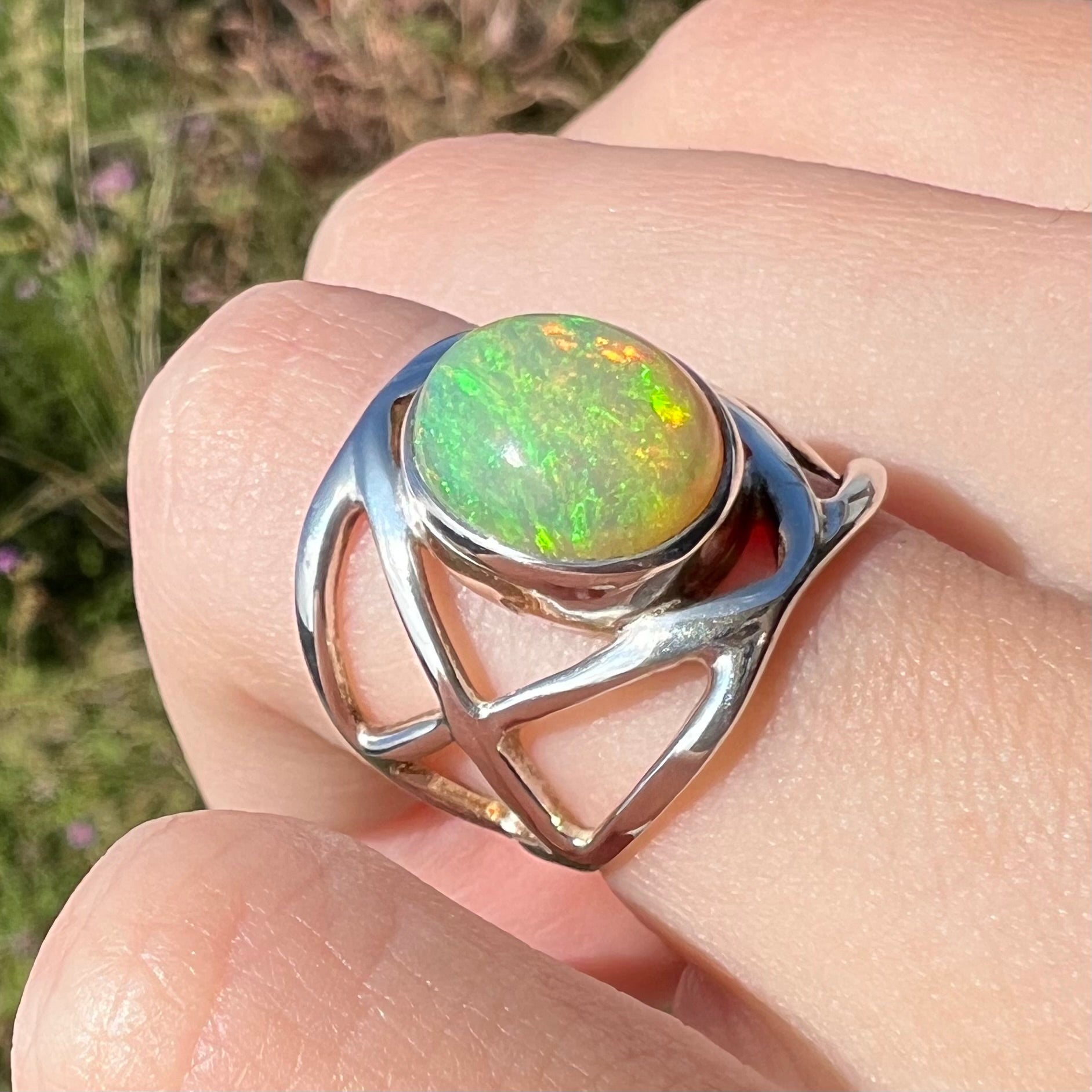 A sterling silver Ethiopian opal ring shown at an angle in natural sunlight while worn on a finger.