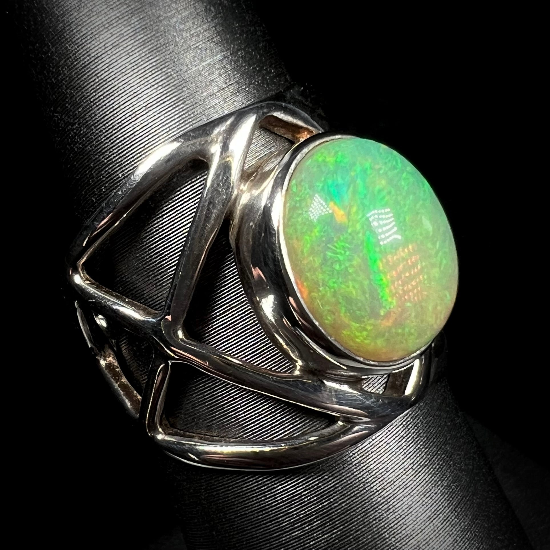 A sterling silver Ethiopian opal ring with green color play, shown at an angle against black background.