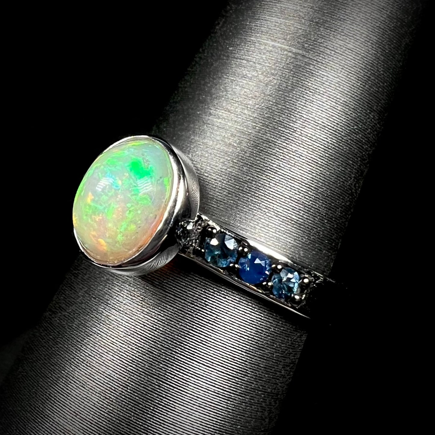 Silver Ethiopian opal ring with blue topaz accents shown at an angle against black background.