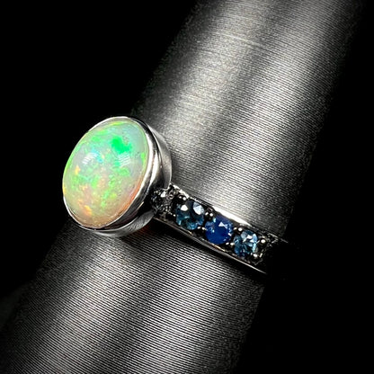 Silver Ethiopian opal ring with blue topaz accents shown at an angle against black background.