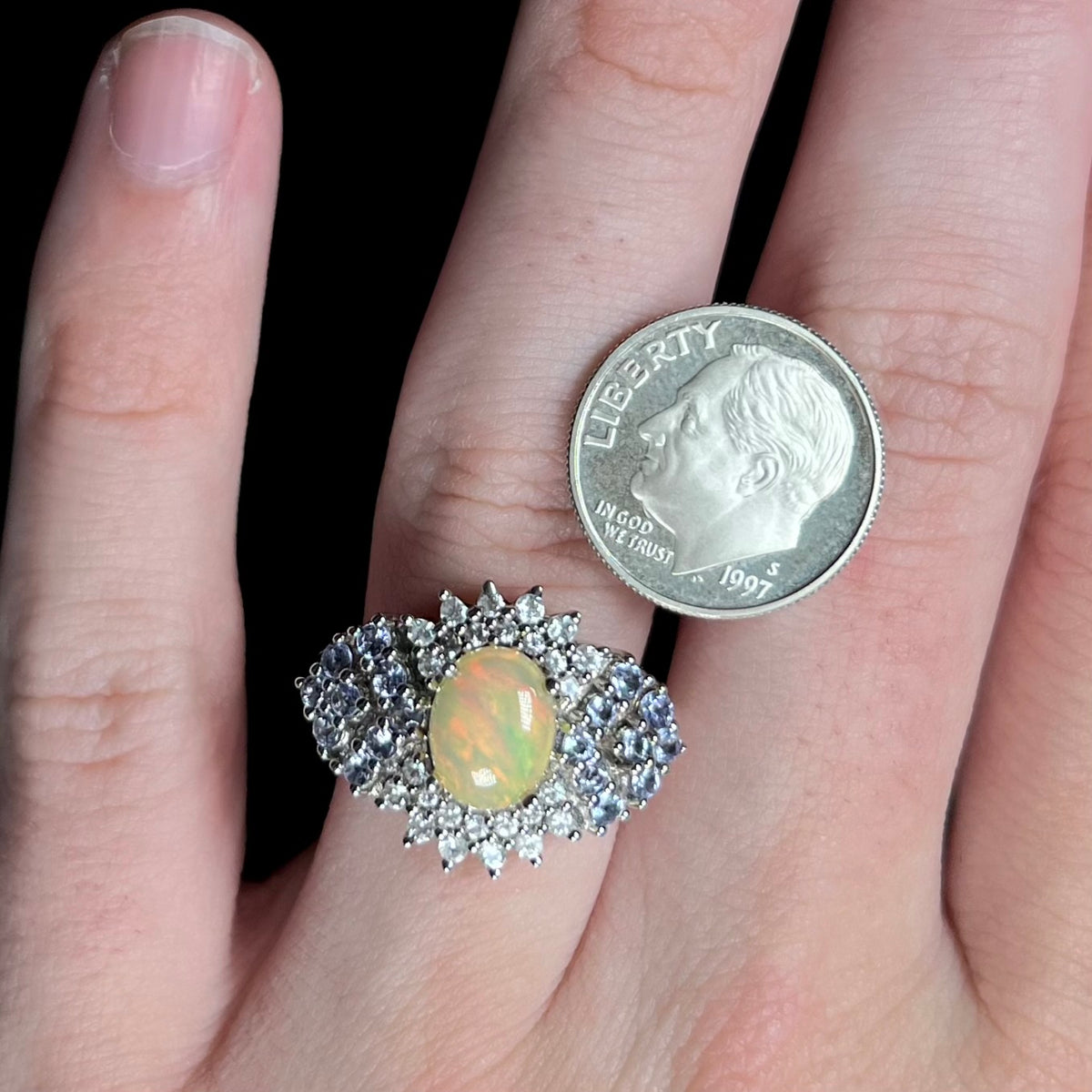 Close-up of hand wearing sterling silver Ethiopian opal and tanzanite cluster design ring next to US dime coin