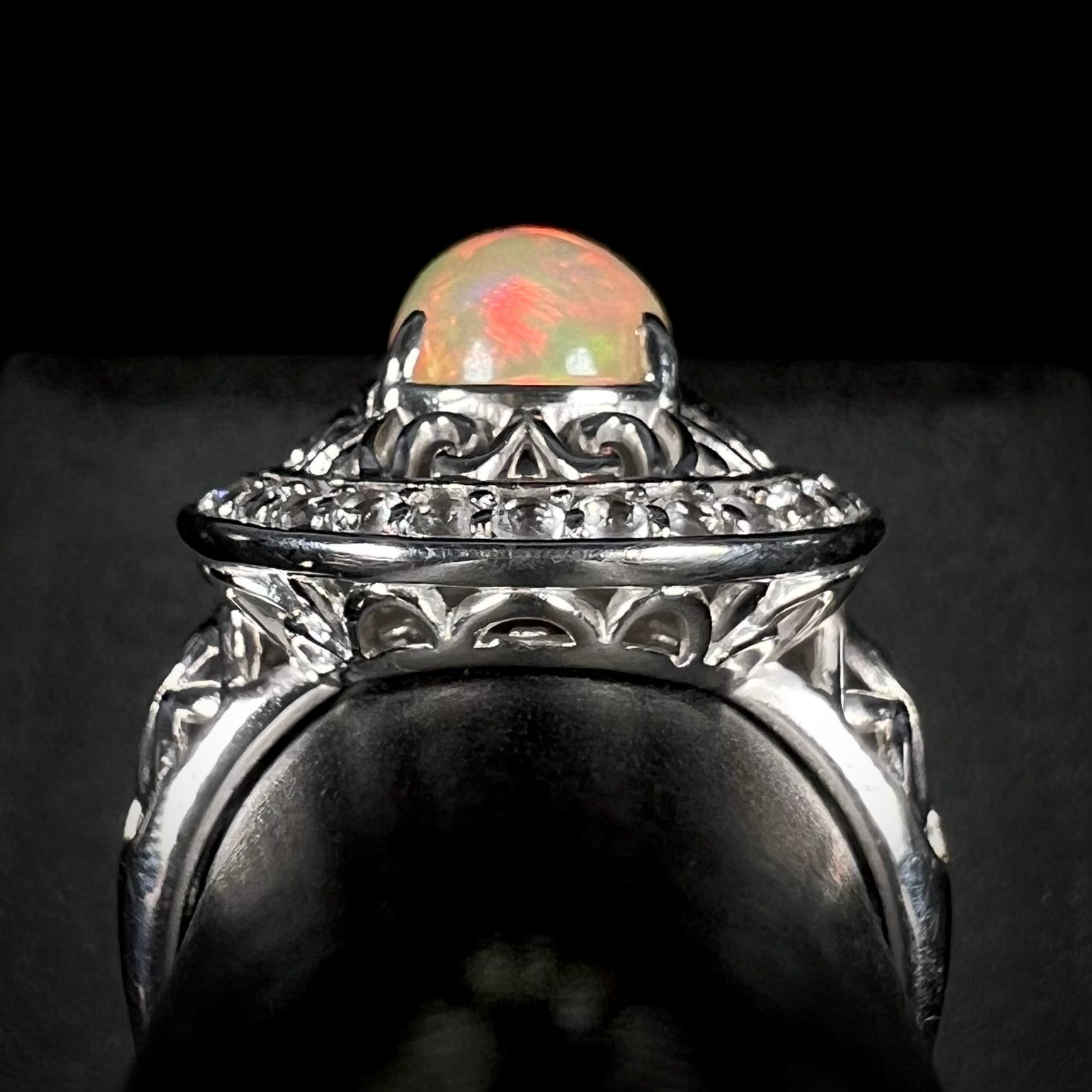 Side gallery of silver filigree opal statement ring against black background.