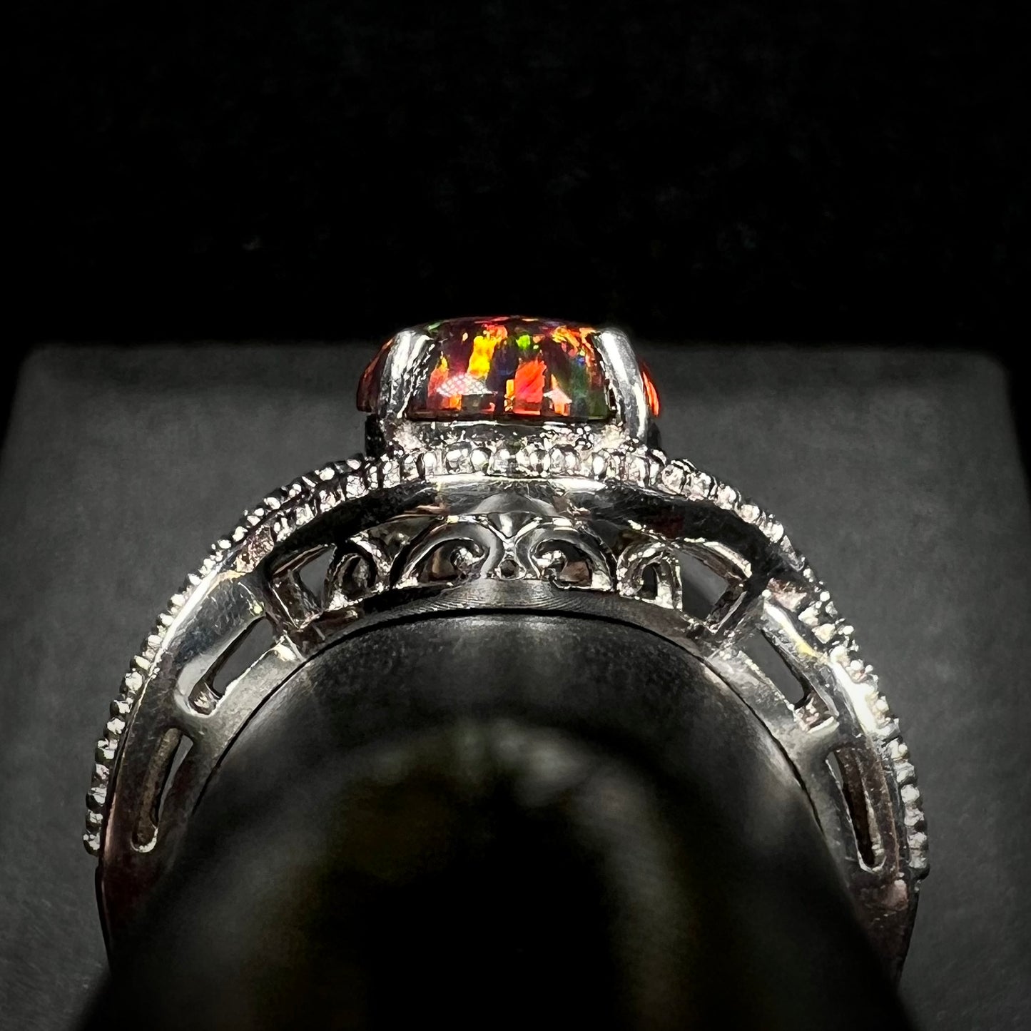 A lab-created black opal solitaire ring in sterling silver with filigree, shown from the gallery view on a ring display.