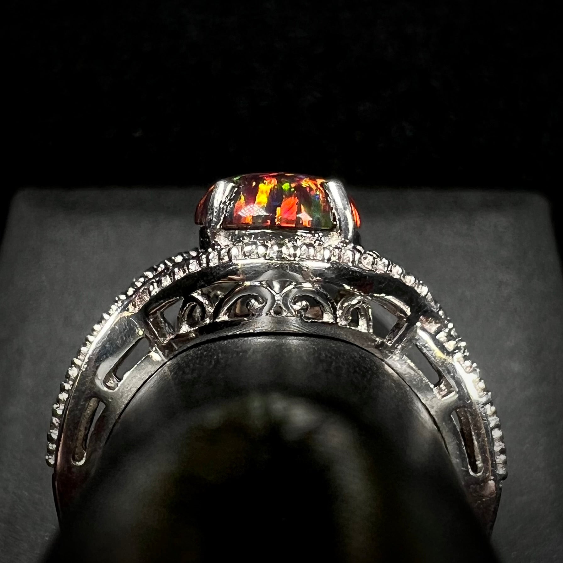 A lab-created black opal solitaire ring in sterling silver with filigree, shown from the gallery view on a ring display.