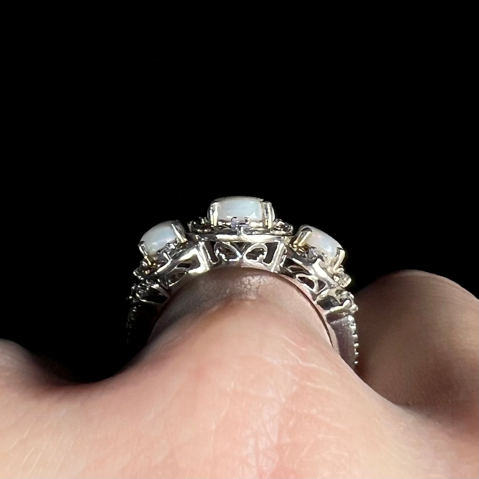 Side profile gallery view of a sterling silver three-stone opal ring on a hand, showing filigree accents along the ring's basket setting.