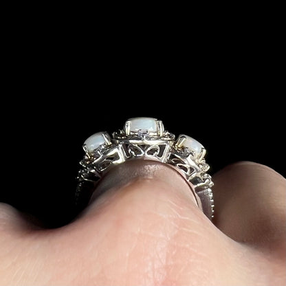 Side profile gallery view of a sterling silver three-stone opal ring on a hand, showing filigree accents along the ring's basket setting.