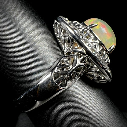 Side view of silver filigree opal ring against a black background.