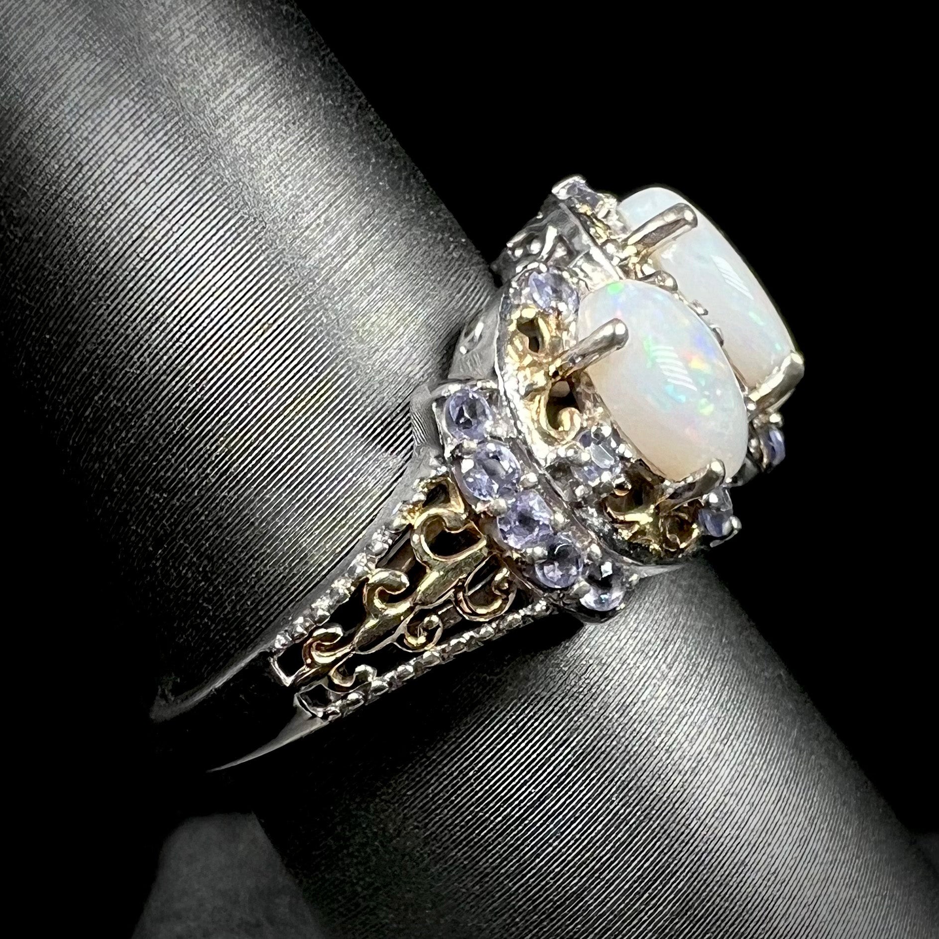 Side profile view of the gold-tone filigree on a sterling silver opal and tanzanite ring, shown on a ring display.