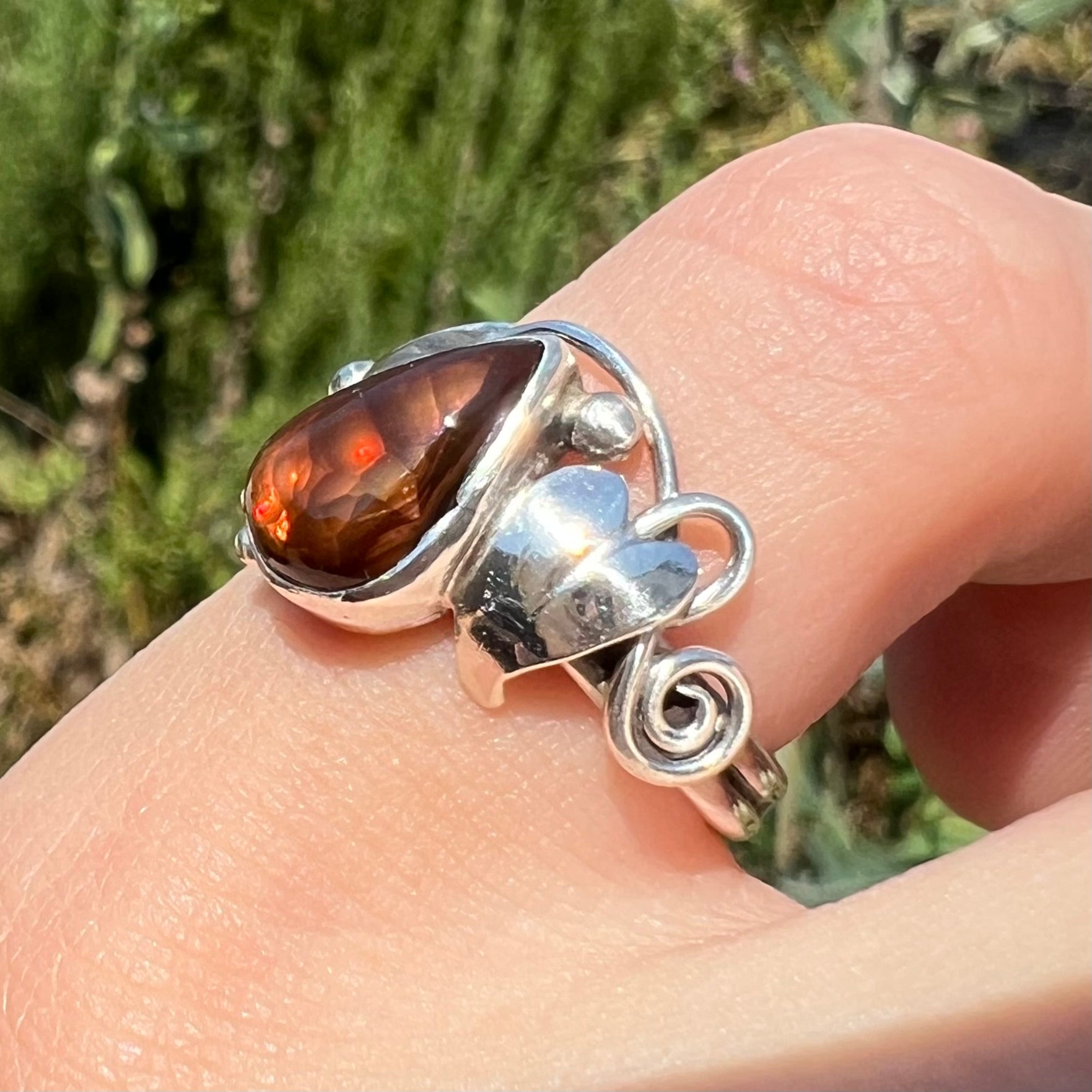 Angled view of a ladies' pear shaped red fire agate ring with a sterling silver leaf design worn in the sunlight.