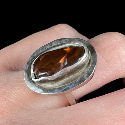 A handmade sterling silver fire agate ring worn on a finger, shown from an angle.