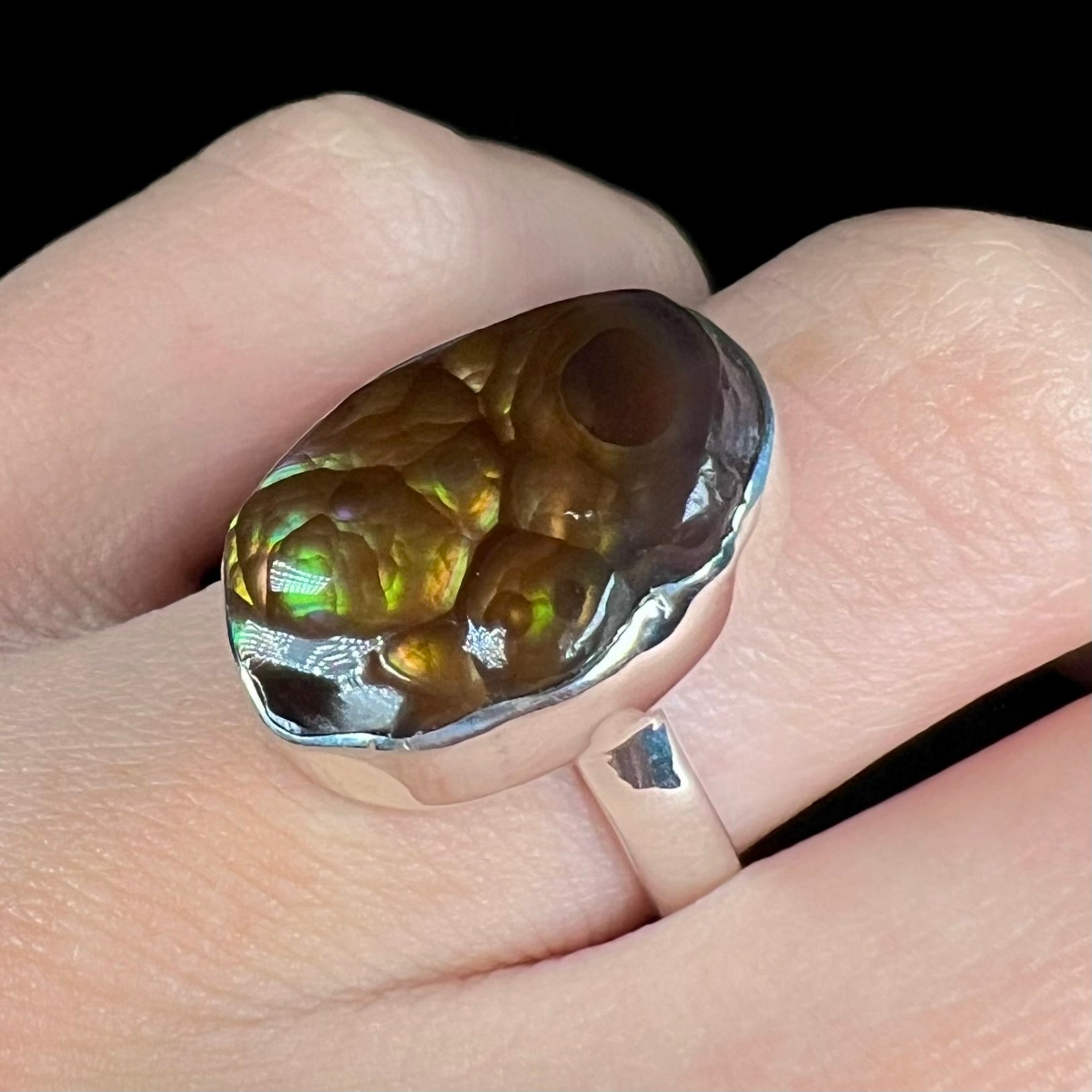 A sterling silver Mexican fire agate ring with green iridescence shown on a finger close-up at an angled view.