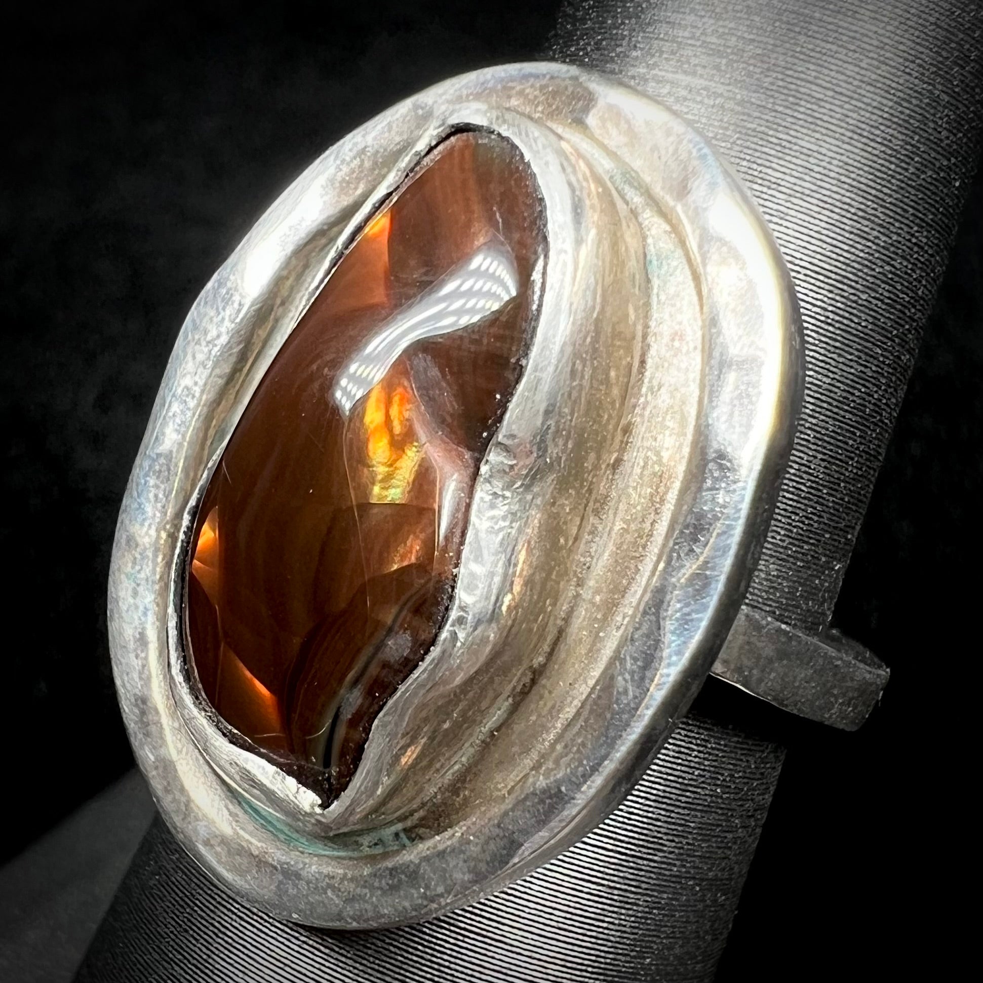 A handmade sterling silver fire agate ring shown at an angle against a dark background.