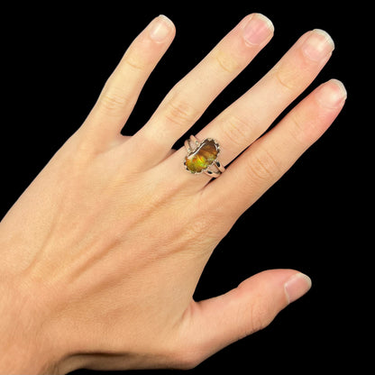 Hand wearing a freeform shaped silver Mexican fire agate ring against black background.
