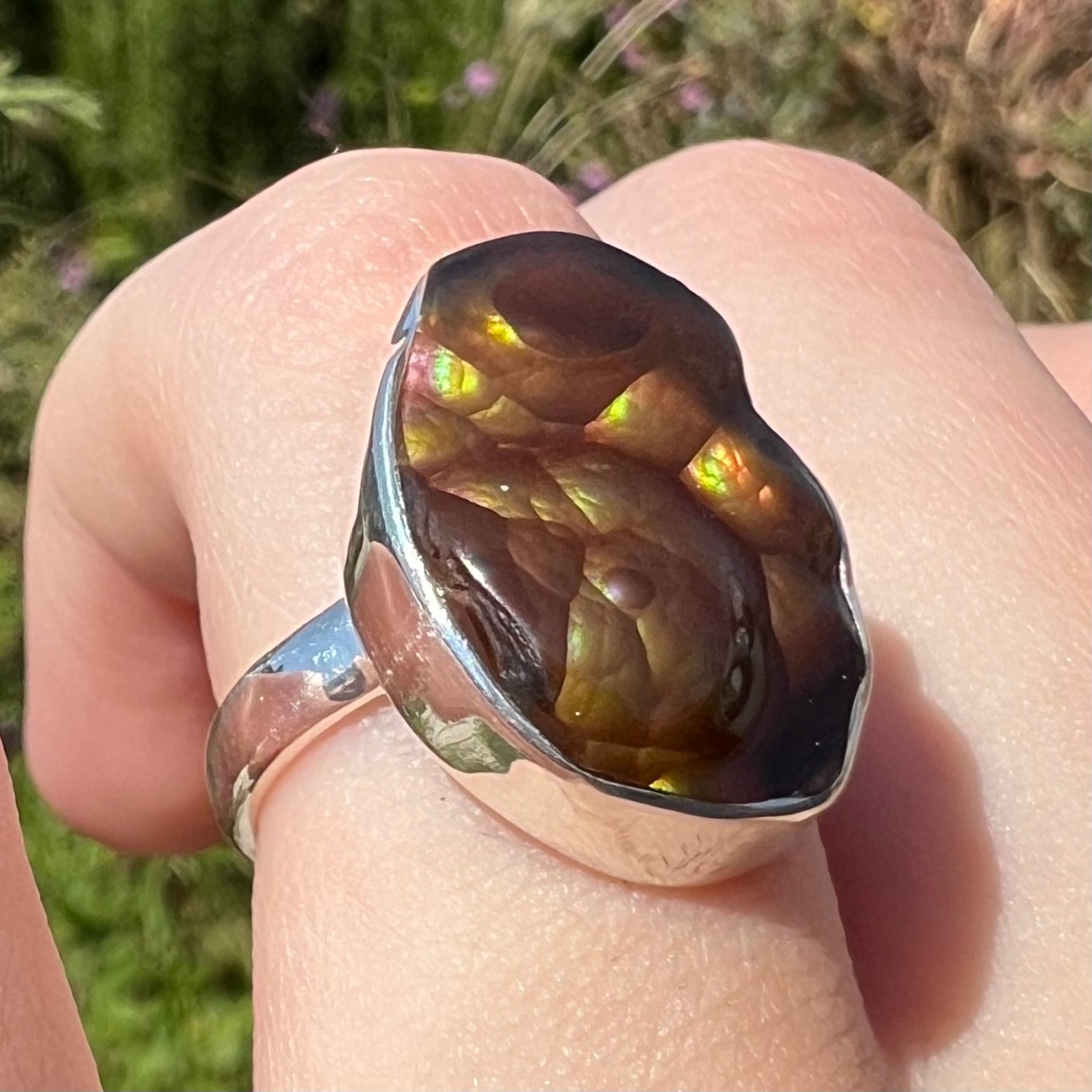 A sterling silver Mexican fire agate ring worn on a hand, shown close-up in the sunlight at an angled view.
