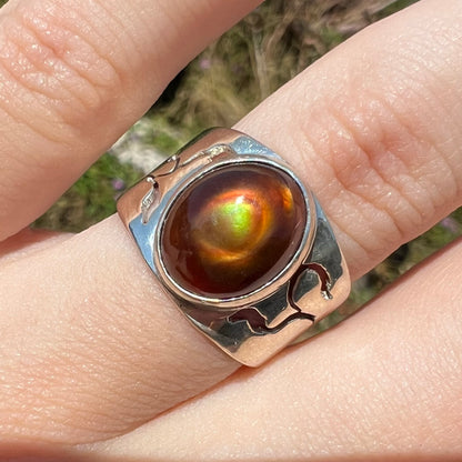 A sterling silver fire agate ring shown on a finger in the sunlight close-up from its front.