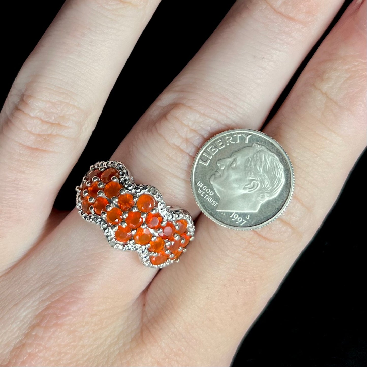 A sterling silver Mexican fire opal and diamond-accented ring, worn on a hand next to a US dime coin for scale.