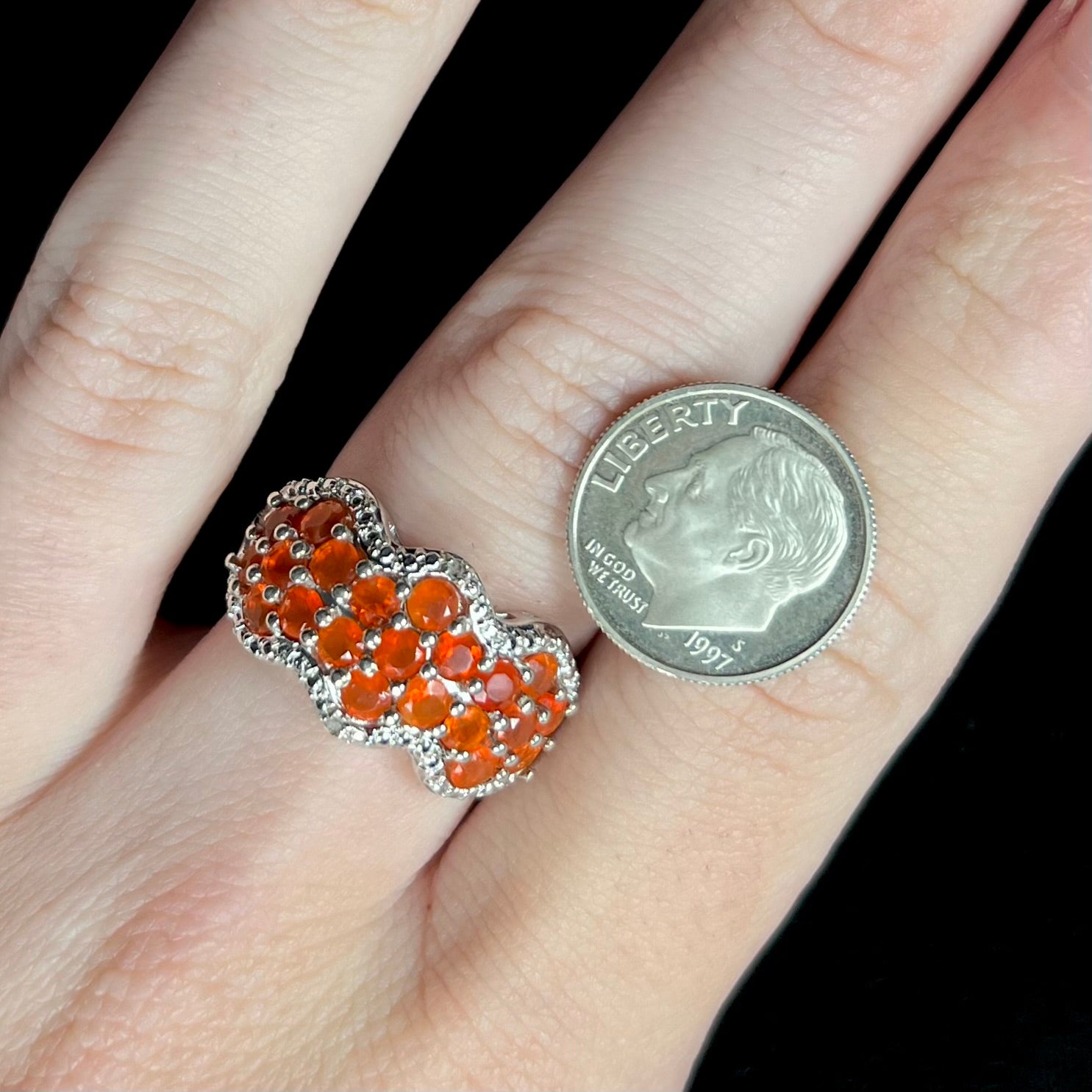 A sterling silver Mexican fire opal and diamond-accented ring, worn on a hand next to a US dime coin for scale.