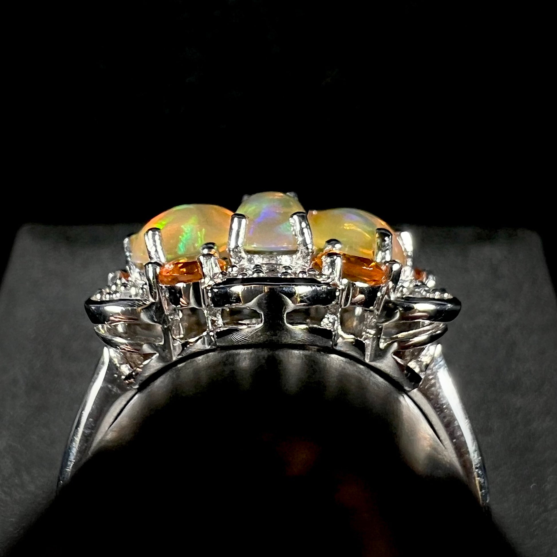Side gallery profile view of a sterling silver fire opal cluster ring against a black and gray backdrop.