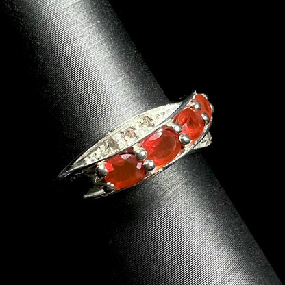 Angled view of silver fire opal and diamond ring against a black background.
