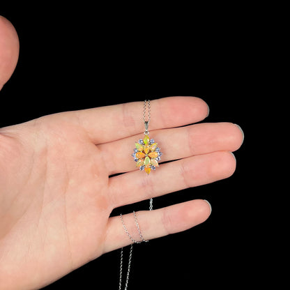A silver fire opal necklace with light blue tanzanite accents, held in a hand against a black background.