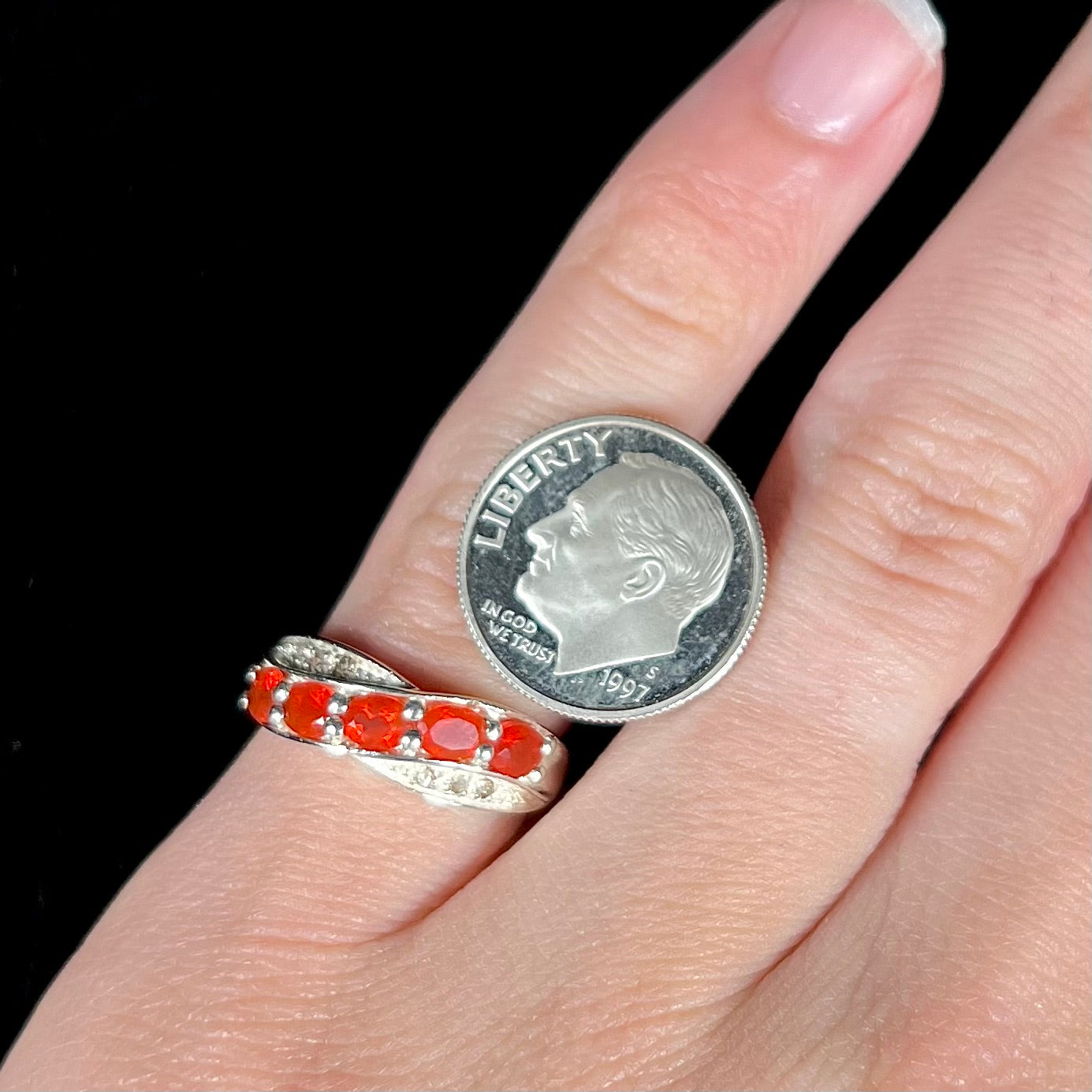 Close-up of silver fire opal ring worn on a pinky finger next to a dime coin.