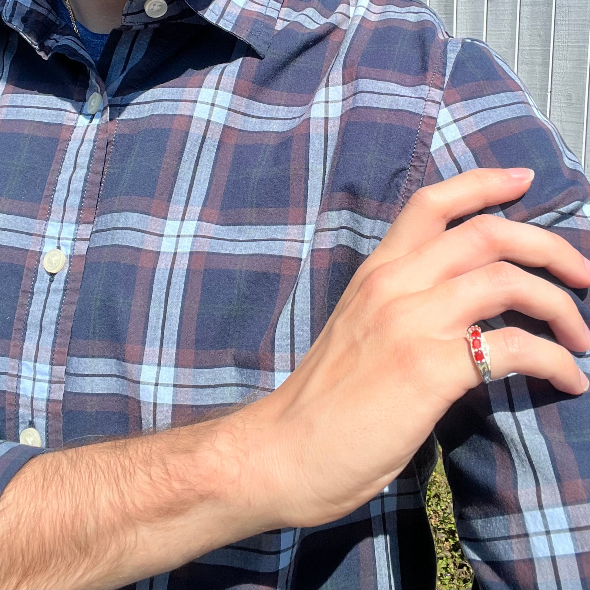 Person wearing a plaid shirt with a hand adjusting the sleeve, wearing a silver fire opal ring in the daylight.