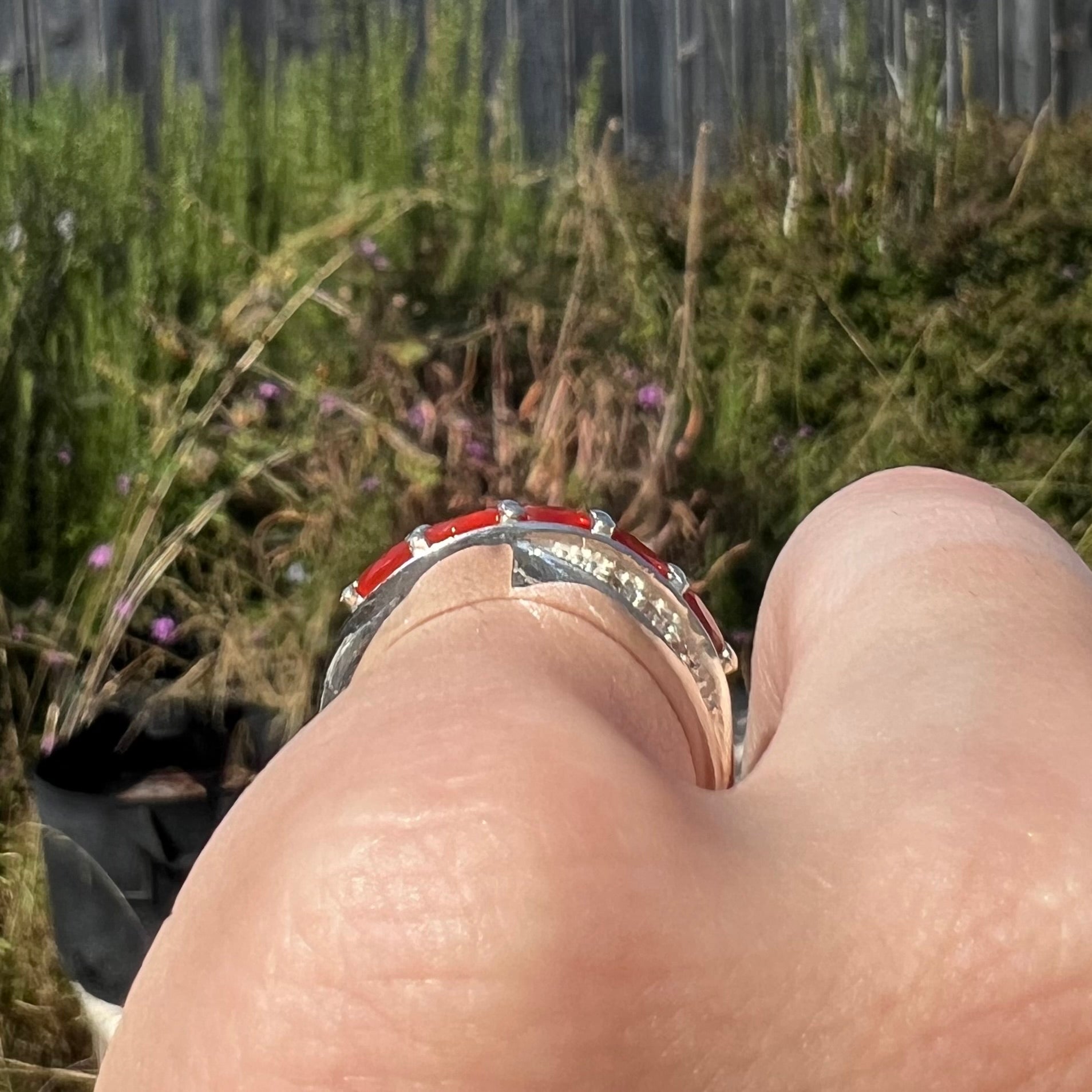 Close-up of a person's finger wearing a silver ring showing side profile view against blurred outdoor background.