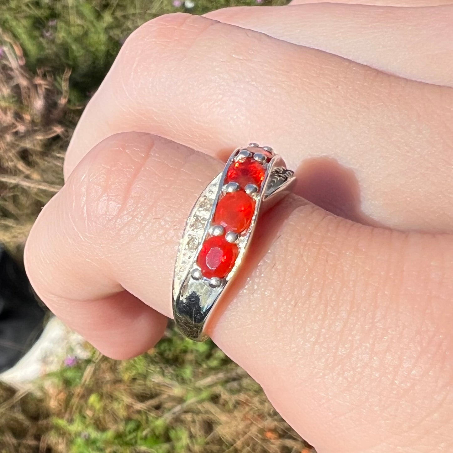 Angled view of silver fire opal ring in sunlight, worn on pinky finger, close-up.