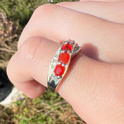 Angled view of silver fire opal ring in sunlight, worn on pinky finger, close-up.