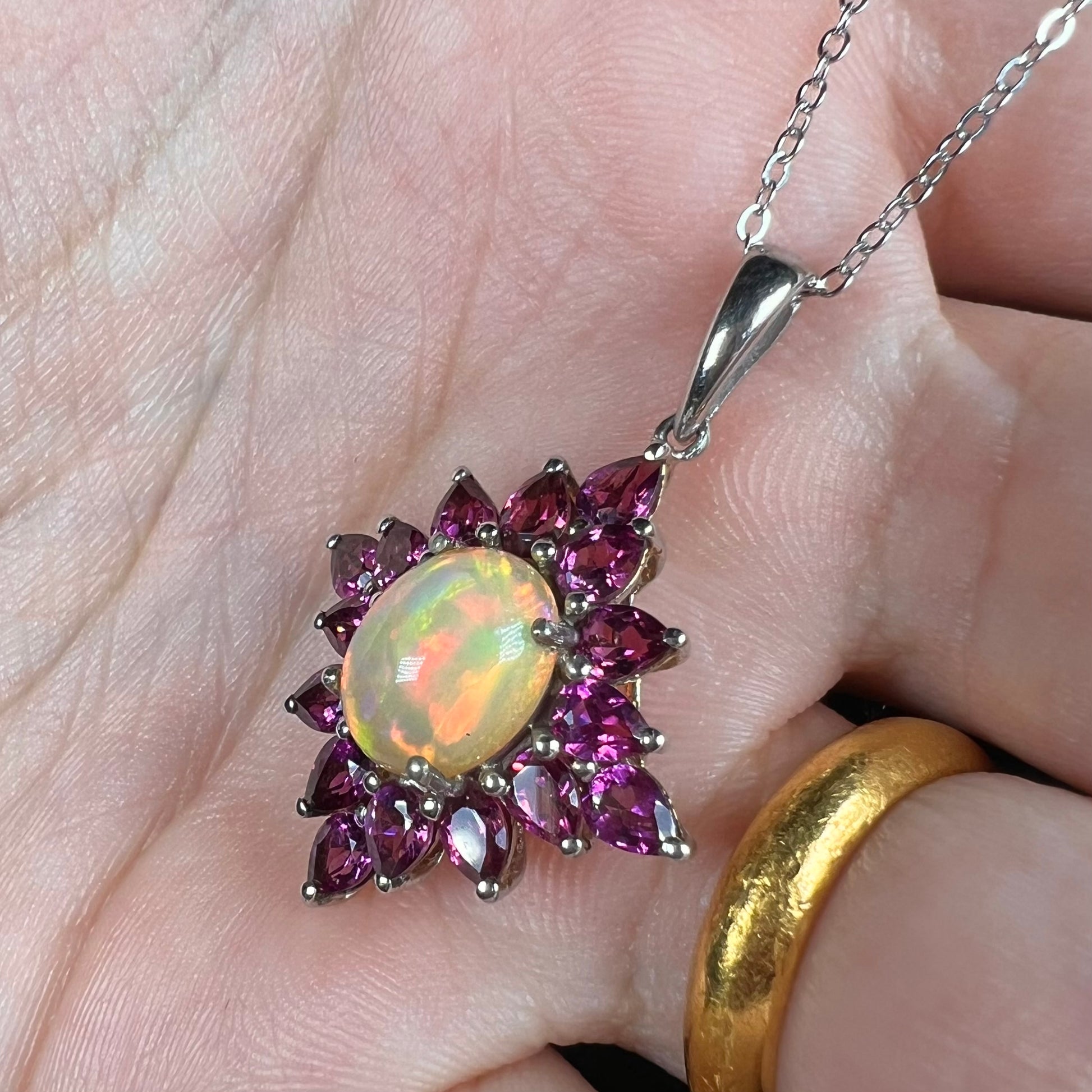 A silver Ethiopian opal and rhodolite garnet spray necklace with red color play, shown in a hand at an angle.