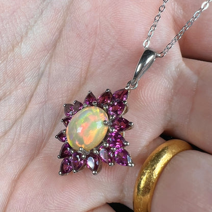 A silver Ethiopian opal and rhodolite garnet spray necklace with red color play, shown in a hand at an angle.