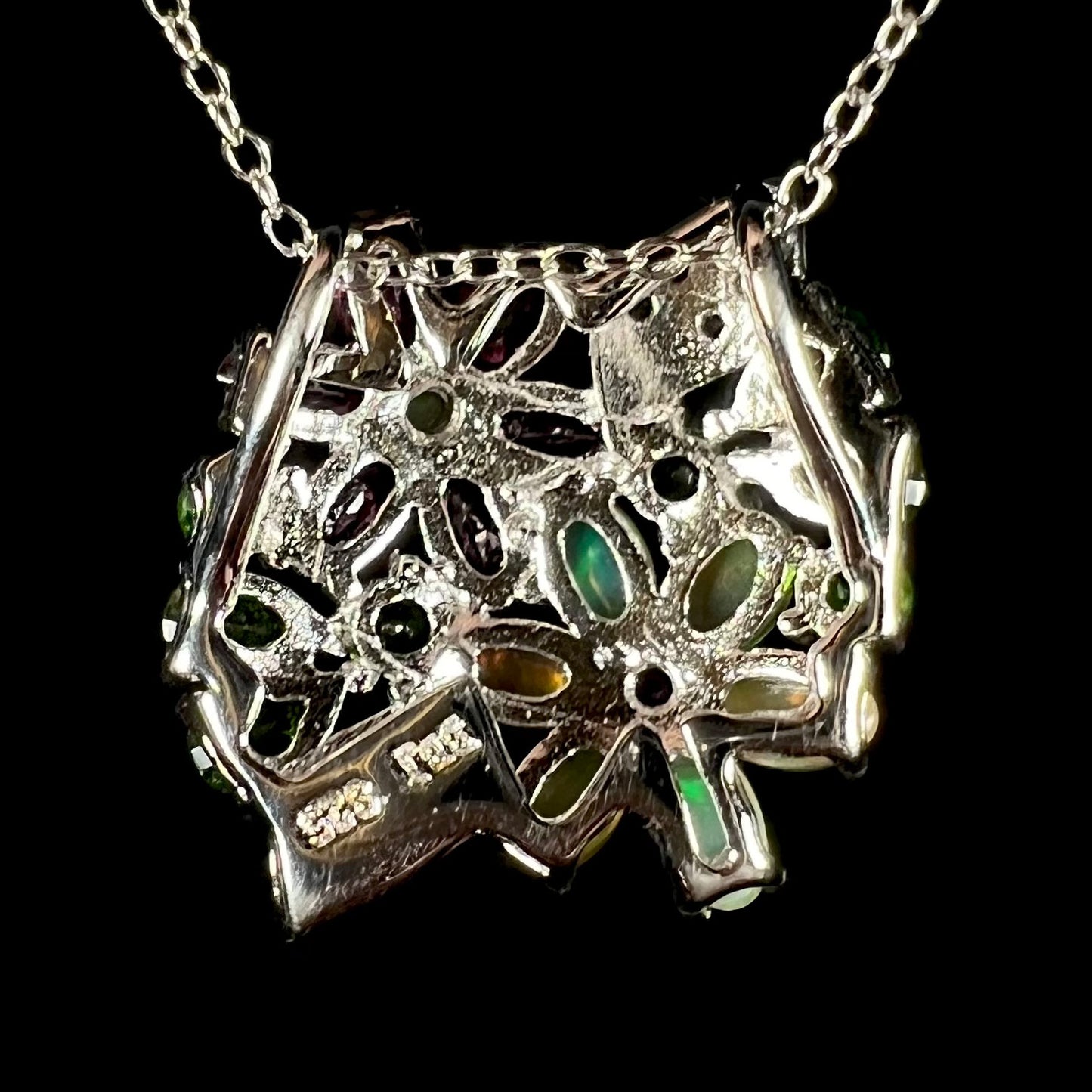 Back side of a silver multi-gemstone cluster flower necklace.  The pendant has a slide bail.