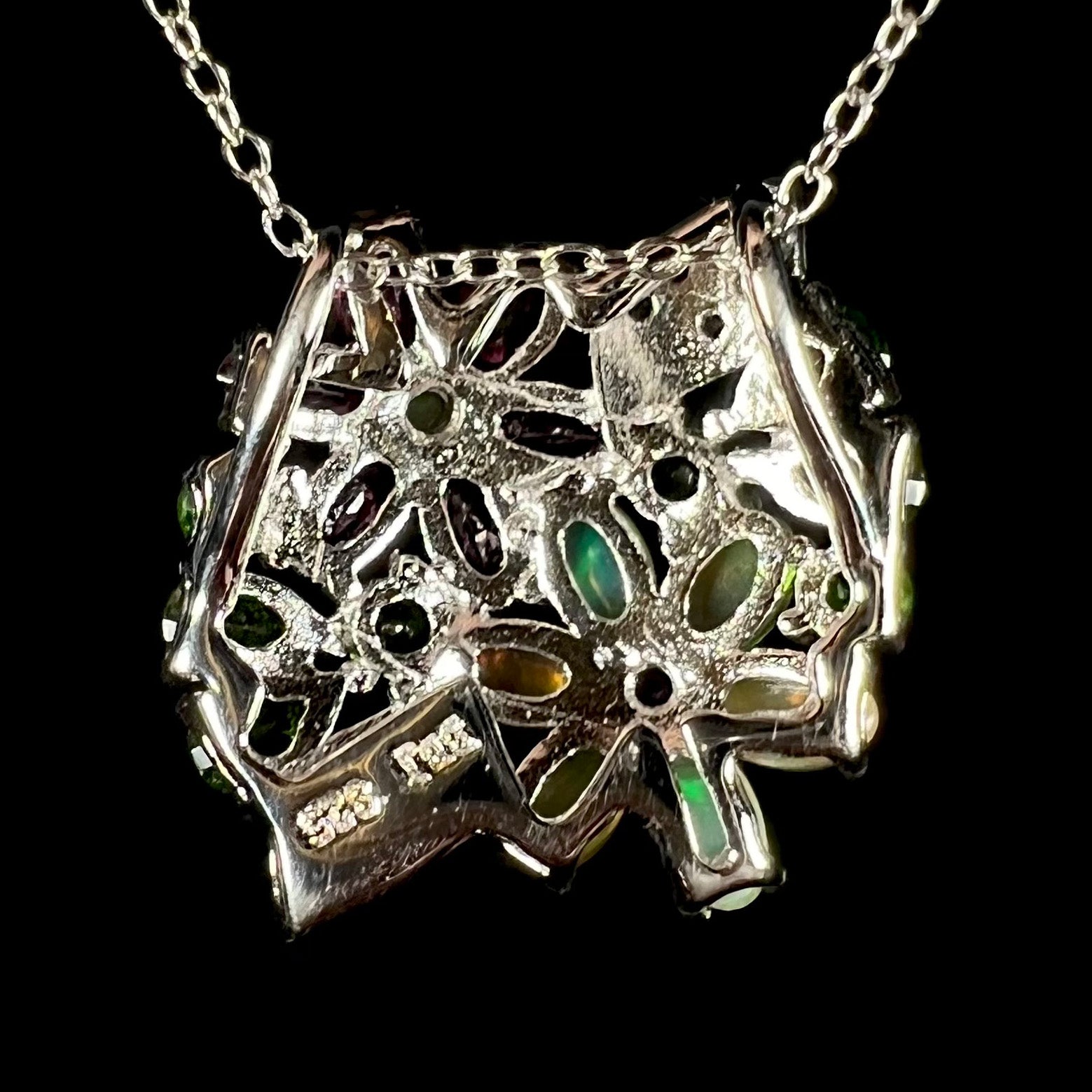 Back side of a silver multi-gemstone cluster flower necklace.  The pendant has a slide bail.