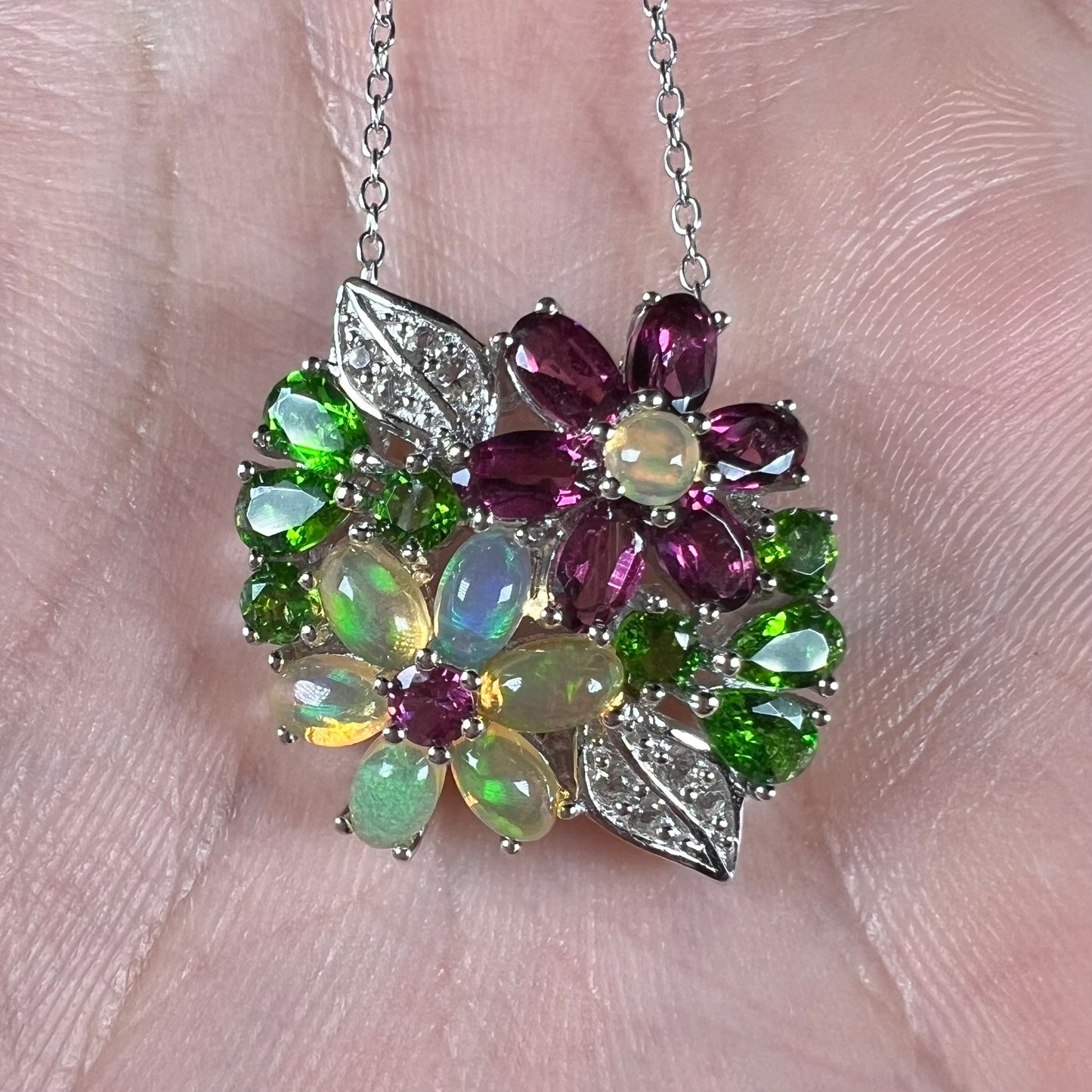 A sterling silver gemstone flower necklace shown close-up in the palm of a hand.