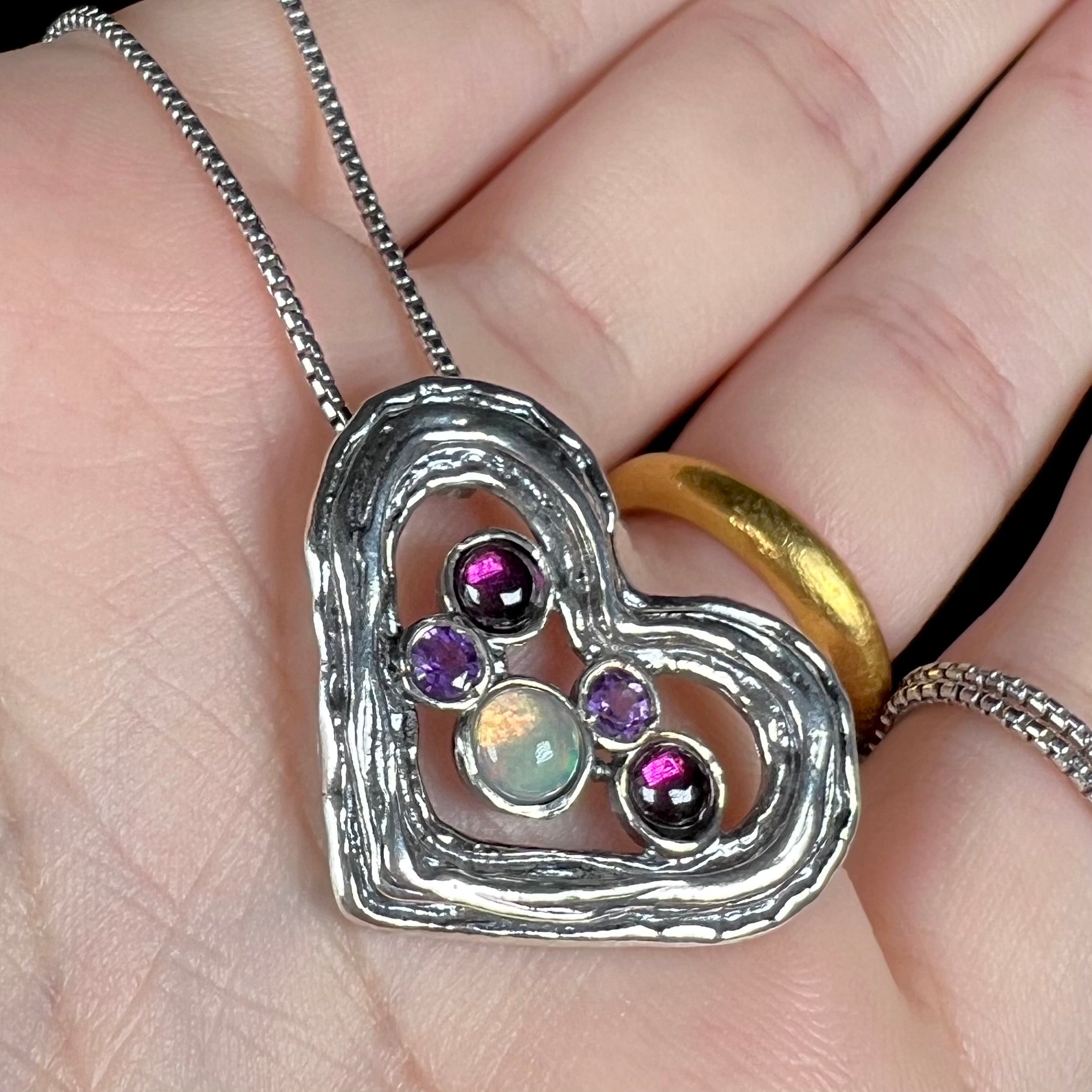 A sterling silver heart necklace set with a round Ethiopoian opal, two amethysts, and two rhodolite garnets.
