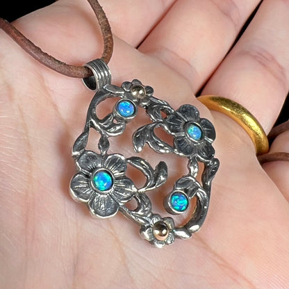 Angled close-up view of a two-tone sterling silver and 14k gold opal dogwood flower pendant held in a hand.