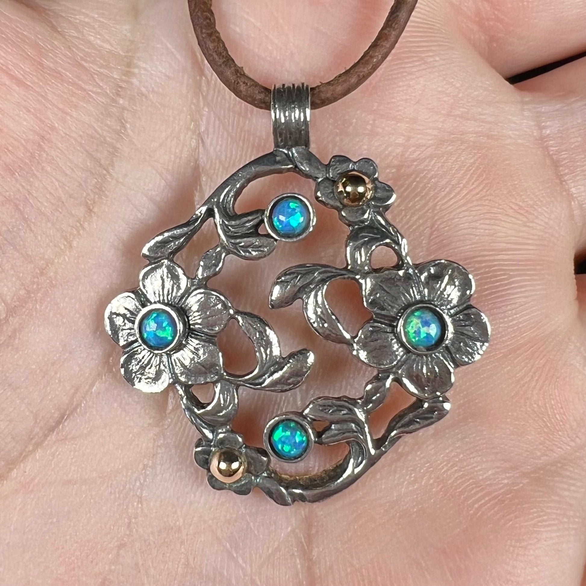 A two-tone sterling silver and 14k gold opal dogwood flower pendant shown in a hand close-up.