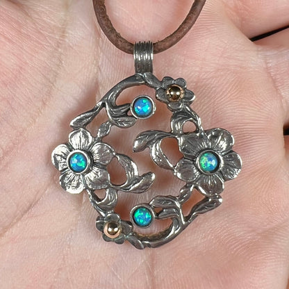 A two-tone sterling silver and 14k gold opal dogwood flower pendant shown in a hand close-up.