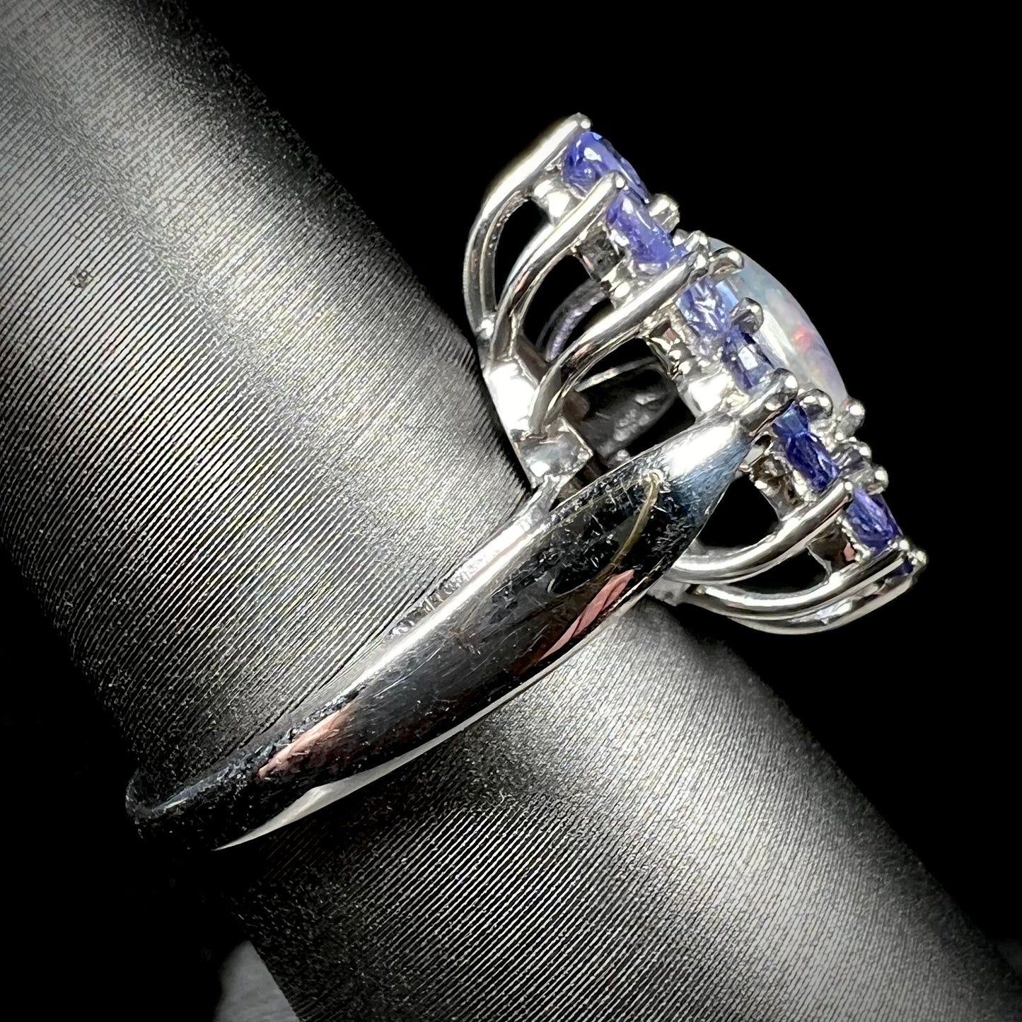 The side view of a silver tanzanite halo ring mounted with an opal triplet.