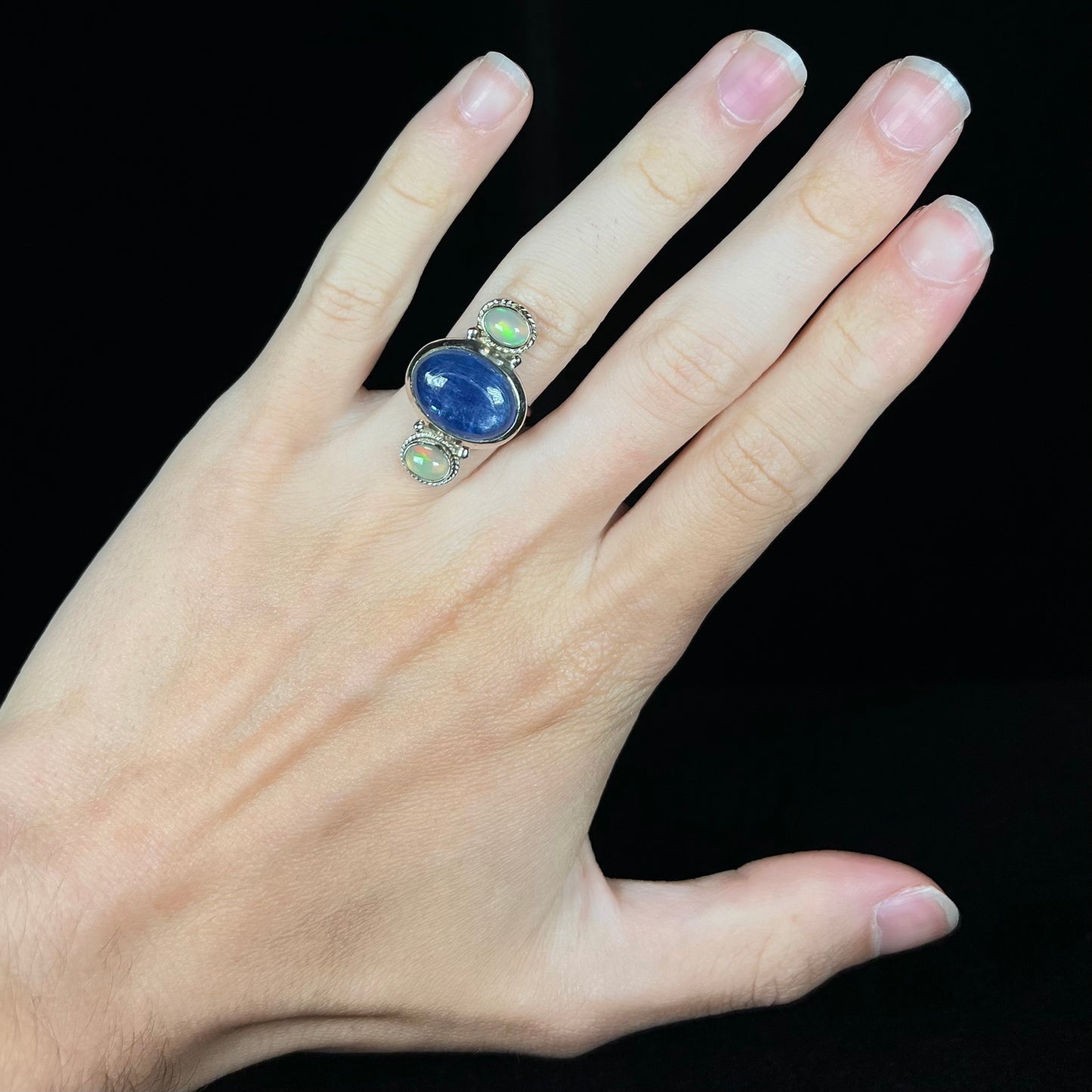 A sterling silver kyanite opal ring worn on a hand against a black background.