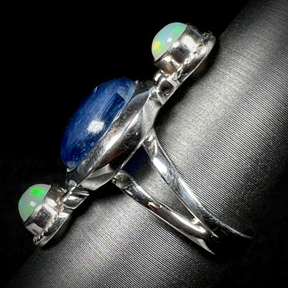 Side view of a silver kyanite and opal ring against a black background.  The ring's split shank is in focus.