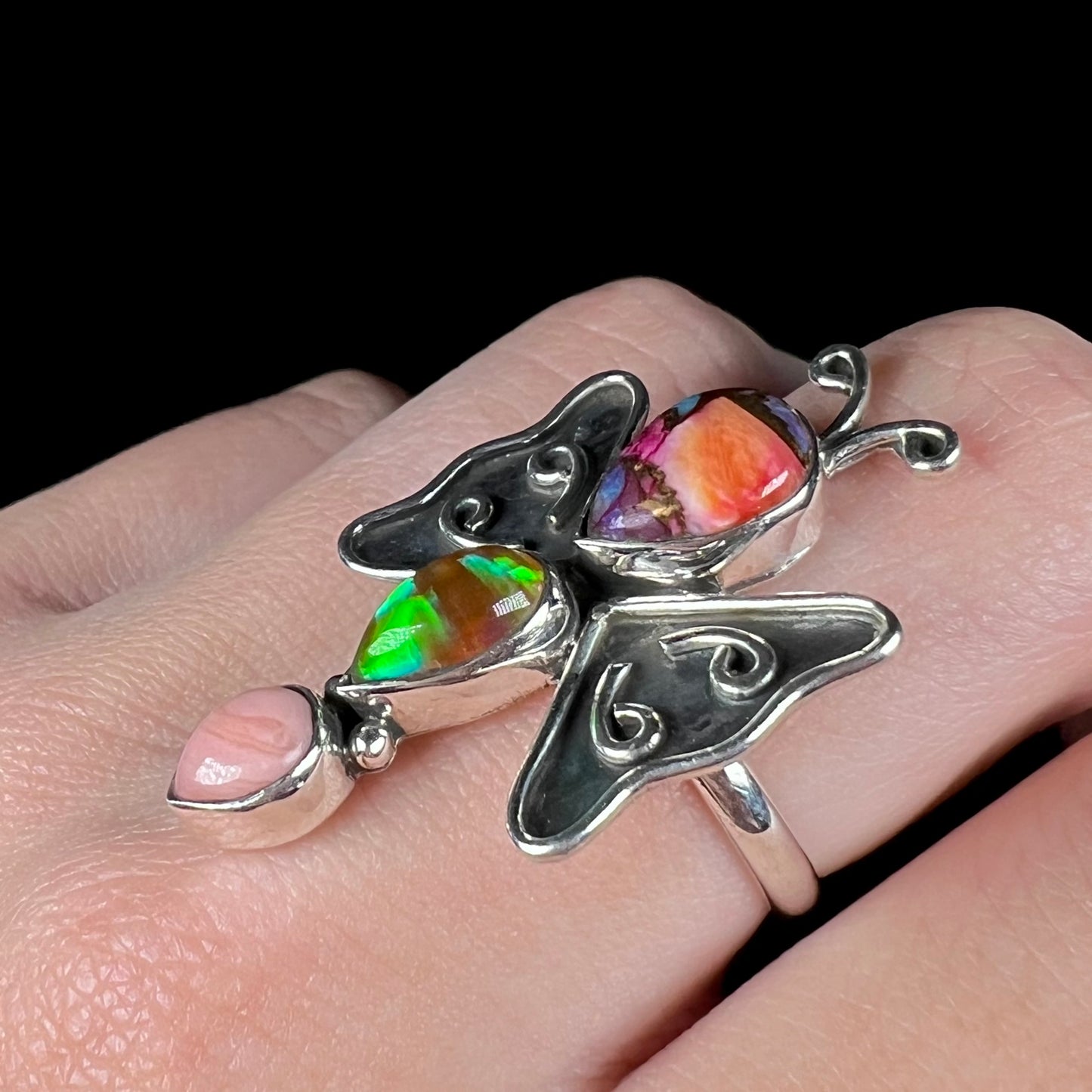 A silver lab-created opal butterfly ring worn on a finger at an angle and shown close-up.