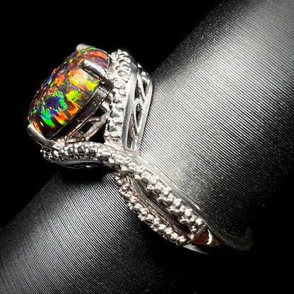 A lab-created black opal solitaire ring in sterling silver, shown from the side on a ring display.